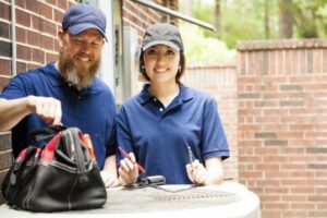 male-female-hvac-technicians-smiling-at-camera-outside-ac-compressor