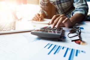 man-types-on-calculator-holds-pencil-with-laptop-and-graphs